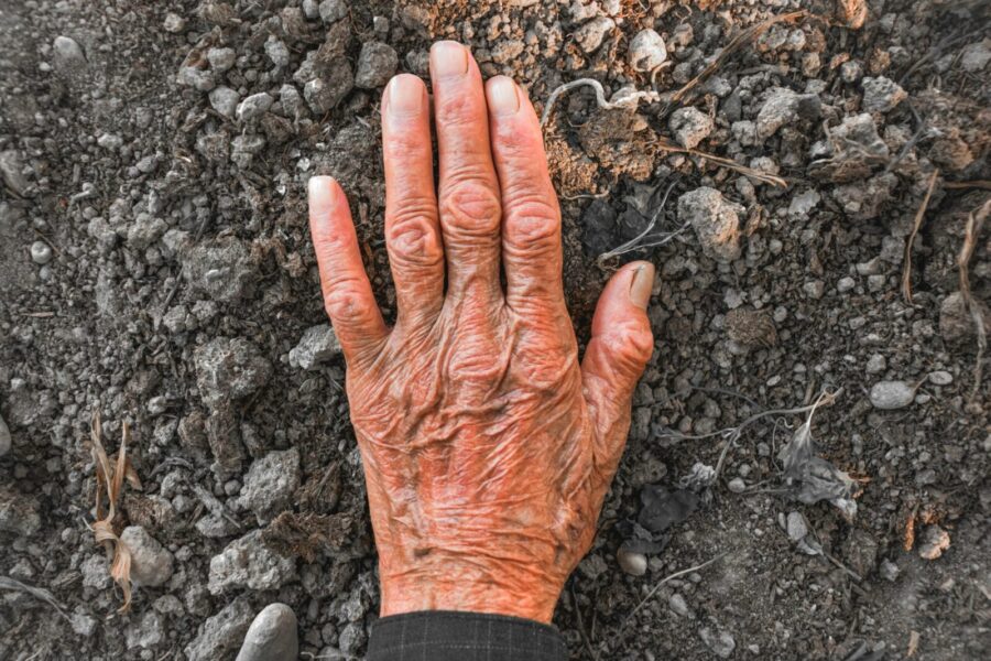 A senior adult hand with wrinkles touching soil, symbolizing connection with nature.