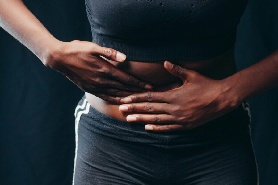 Close-up of a person pressing hands on abdomen, indicating discomfort or pain, against a black background.
