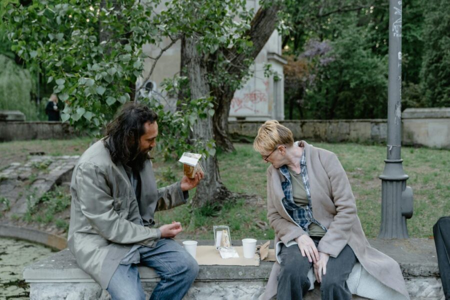 Two individuals sitting in a park, engaged in conversation while sharing a meal on a stone bench.