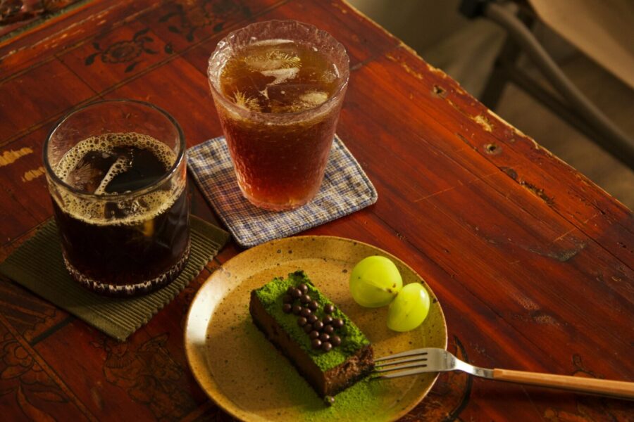 Two iced coffee drinks with a green tea cake and grapes on a rustic table setting.